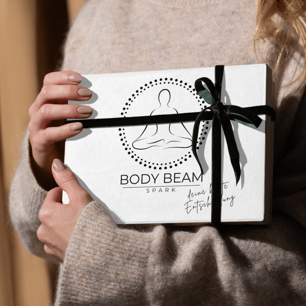 BODY BEAM SPARK Geschenkbox mit schwarzer Schleife, edel verpackt und präsentiert von einer Person in einem gemütlichen Pullover.